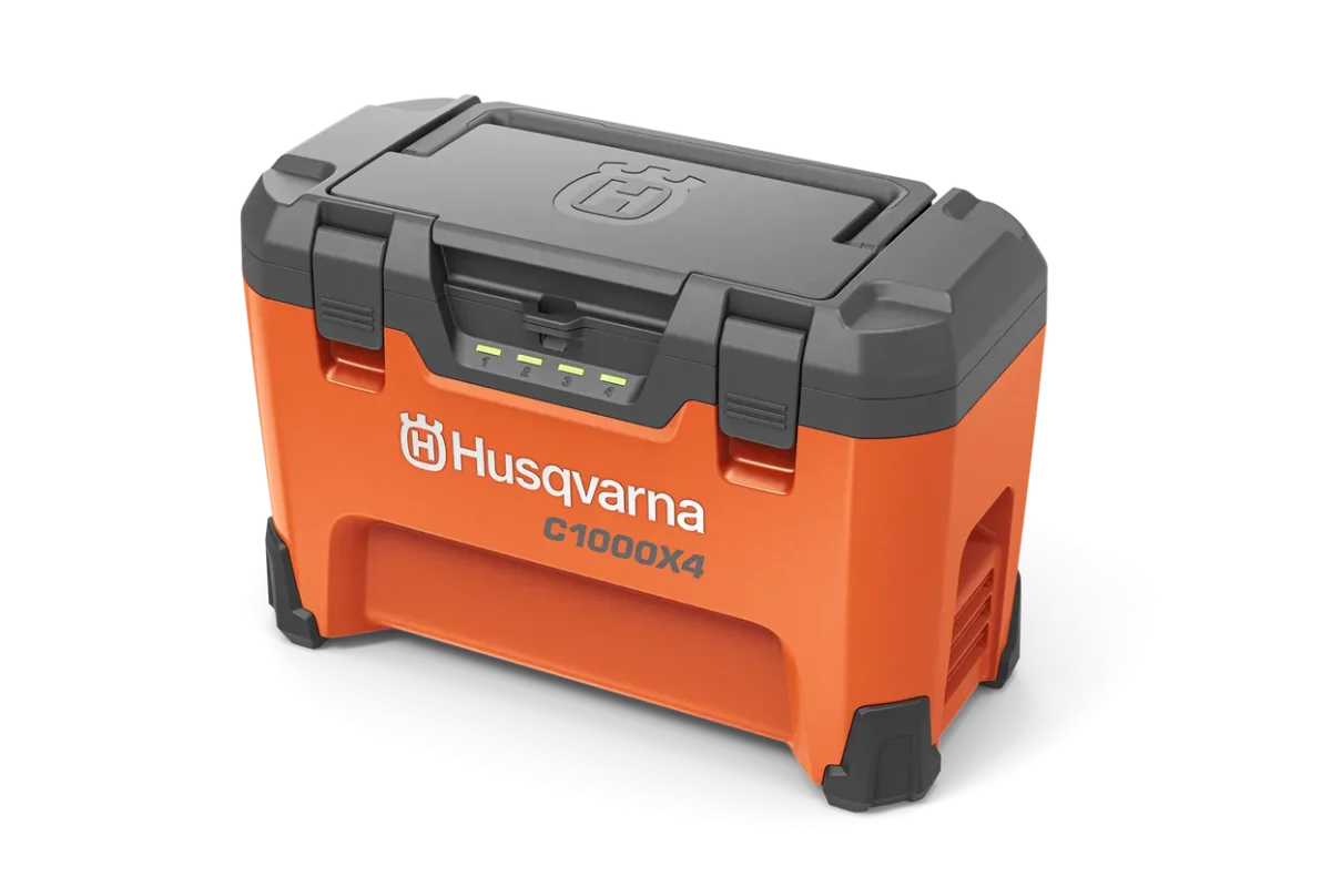 Husqvarna C1000X4 multi-bay battery charger in bright orange and dark gray, featuring a sturdy compact design with four LED charging indicators on the front, ergonomic foldable lid handle, and durable bumpers on the corners.